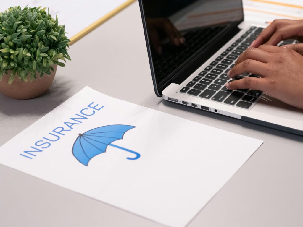 pexels-photo-7688374-7688374 Close-up of hands typing on laptop with an insurance document visible on the desk.